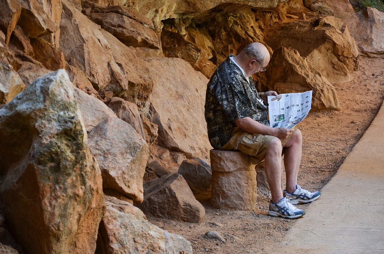 Elderly man sitting on the edge of a rock reading a newspaper